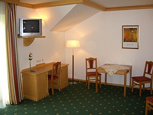 Gasthof Kögl 'Zum Liederfürst', © Gasthof Kögl Zum Liederfürst Hotel room with green carpet, wooden furniture, table, chairs and TV.