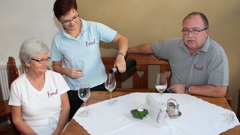 Family, © Weinbau Proisl Three people are sitting at a table, a woman is pouring wine.
