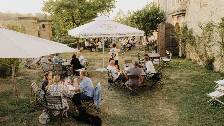 Garden, © Ella Szechenyi People sit at outdoor tables in a garden with parasols.