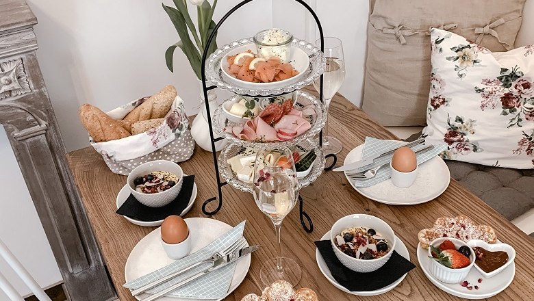 Lovingly prepared breakfast variations, © Mille Fleurs A laid breakfast table with etagere, bread rolls, eggs, muesli and fruit. Decorated with tulips and cushions.