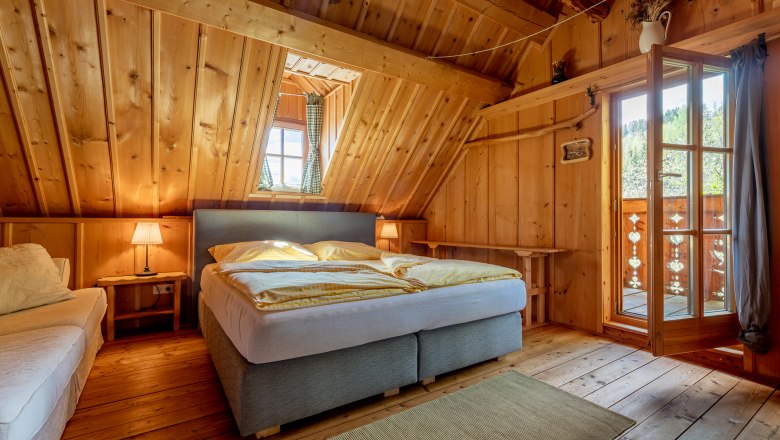 Kronaushof, © Wiener Alpen / Christian Kremsl Bedroom with wood paneling, double bed, carpet and open door to the balcony.