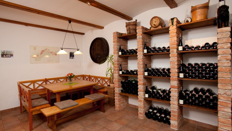 Wine cellar with tasting corner, © Gebetsberger A wine cellar with a table and benches for tasting, surrounded by wine racks full of bottles.