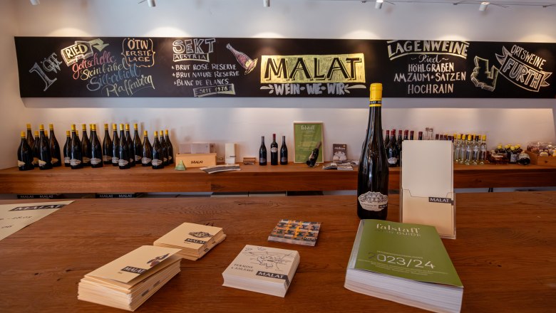 MALAT Winery and Hotel, © Niederösterreich Werbung / Maximilian Pawlikowsky Interior view of a wine store with wine bottles and brochures on wooden tables.