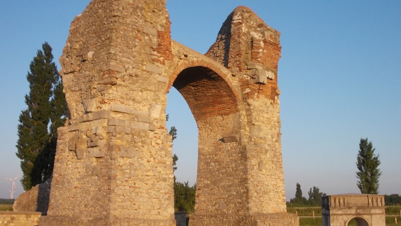 Heidentor, Petronell-Carnuntum, © Donau Niederösterreich Pagan Gate in Petronell-Carnuntum, an ancient Roman monument made of stone with an arch, surrounded by green countryside.