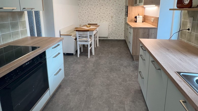 Kitchen, © Waltraud Forstner Modern kitchen with gray cabinets, wooden accents and a dining table. A geometric lamp on the ceiling.