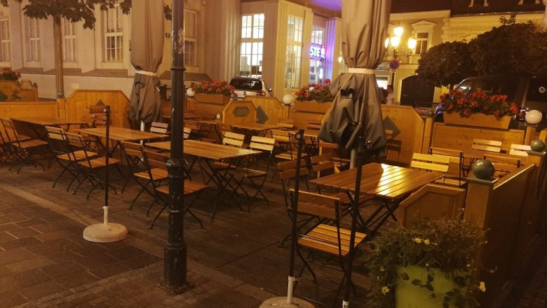 Adlerbräu outdoor area, © Roman Zöchlinger Outdoor area of a restaurant with empty wooden tables and chairs, surrounded by plants and lanterns at night.