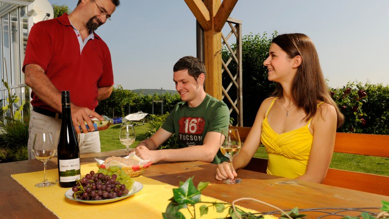 A glass of wine at the Krappel, © Gästehaus Krappel A man pours wine for two people at an outdoor table.