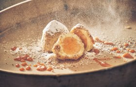 Iced apricot dumplings, © Niederösterreich Werbung/Andreas Hofer Iced apricot dumplings with powdered sugar and apricot sauce on a sieve.
