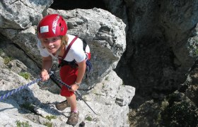 Alpine School Peilstein, © Alpinschule Peilstein Person climbing on rocks with red helmet and rope.