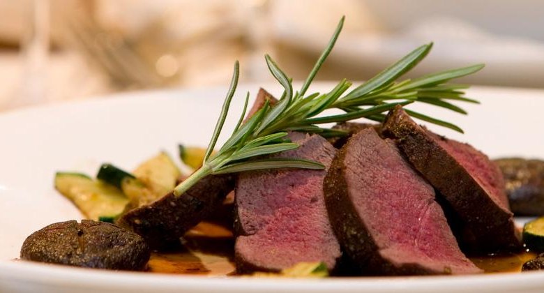 Gourmet menu, © F. Bläuel GesmbH A gourmet dish with pink roasted meat, garnished with rosemary, on a plate with zucchinis and mushrooms.