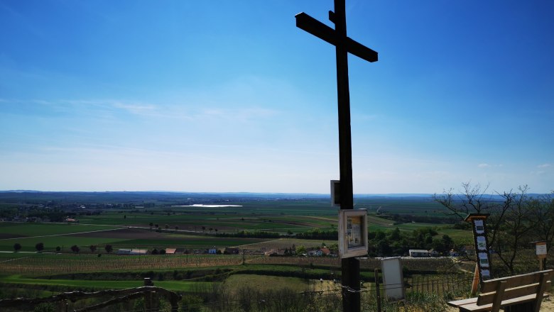 Freedom cross with a wonderful distant view, © Weinstraße Weinviertel A large wooden cross on a hill overlooking a vast landscape under a blue sky.