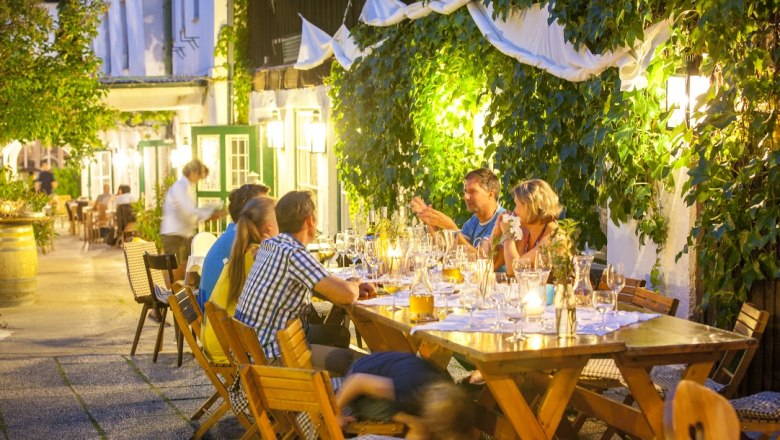 Gebeshuber, © Gebeshuber People sit at a long table outside, surrounded by plants and lights.