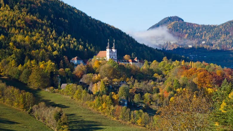 Autumnal Maria Schutz, © Fam. Auer GmbH Autumn landscape with church in Maria Schutz, surrounded by colorful trees and hills.