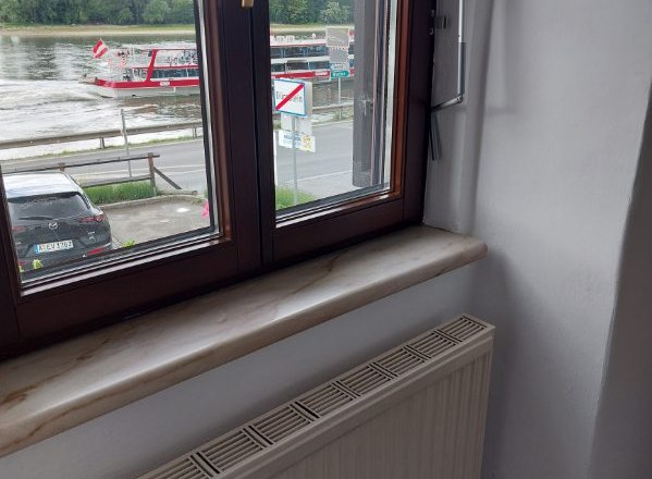 Guest room Weixelbaum, © Familie Weixelbaum View from a window onto a river with a passing boat and a parked car.