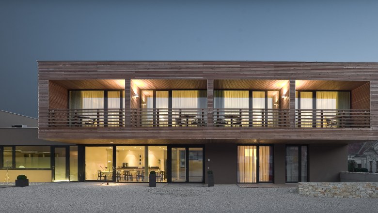 House night, © Rosenberger Modern two-story house with wood paneling and large windows with night lighting.