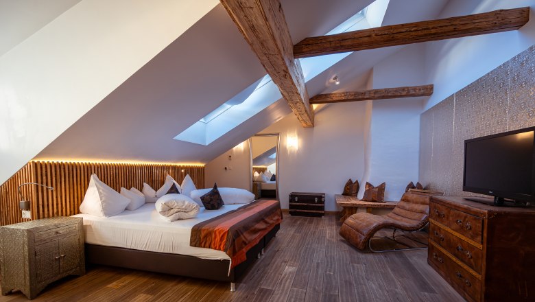 Hotel Landhaus Moserhof, © Niederösterreich Werbung / Maximilian Pawlikowsky Cozy hotel room with wooden beams, skylights, large bed and leather armchair.