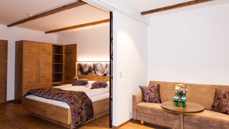 Room view, © Martina Siebenhandl Comfortable hotel room with wooden furniture, double bed, sofa and small table.