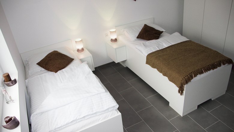 UHL workers' quarter, © Arbeiterquartier UHL Two single beds in a modern, bright room with white furniture and brown ceilings.