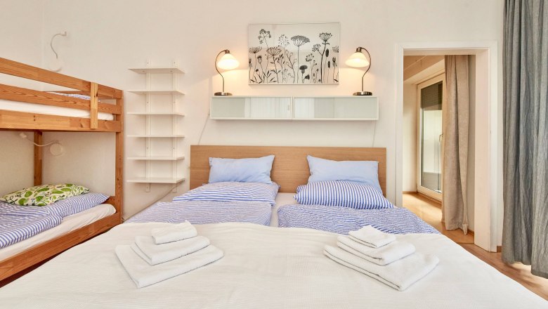 Top 2 - Bedroom, © VP FeWo OG Bedroom with double bed, bunk bed, blue bed linen and towels.