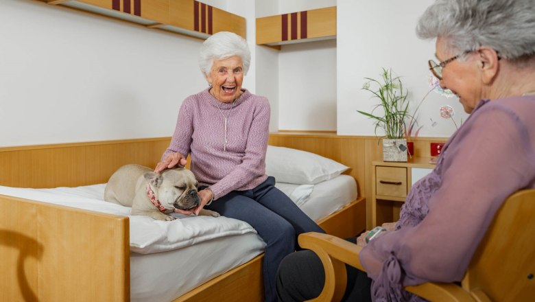 In the room, © ÖJAB Waldpension - Christian Kremsl Two older women in a room, one petting a dog on the bed.
