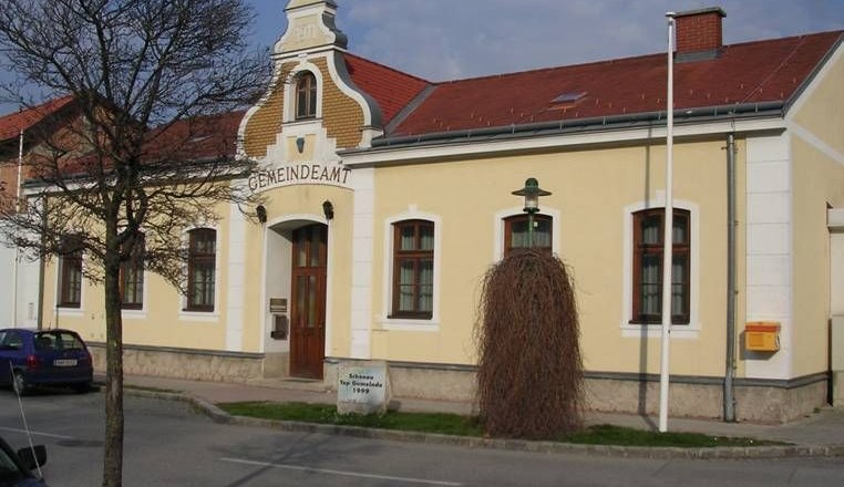Schönau, © Schönau Yellow building with the inscription 'Gemeindeamt', red roof, tree and lantern in front of it.