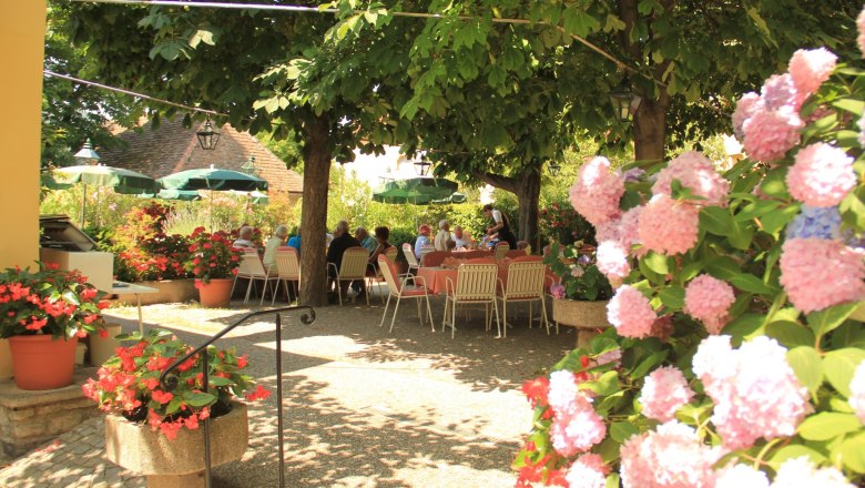 Flower garden, © Schendl A garden with blooming hydrangeas and people sitting at tables under trees.