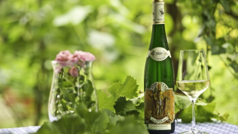 Wine from the Loibnerhof, © Rita Newman Wine bottle and glass on table with flowers and leaves in the background.