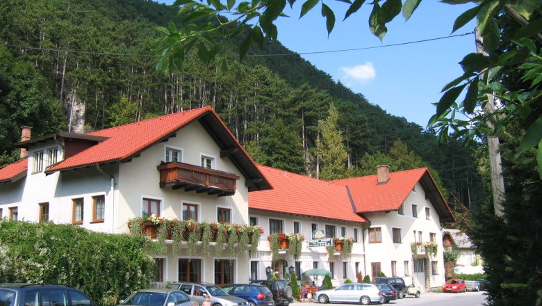 Inn, © Gasthof zur Bruthenne A traditional inn with red roofs and flower boxes, surrounded by woods and parked cars.