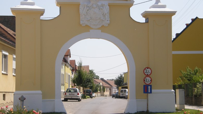 Upper gate, © Marktgemeinde Trautmannsdorf/L. Yellow gate with coat of arms spanning a street.
