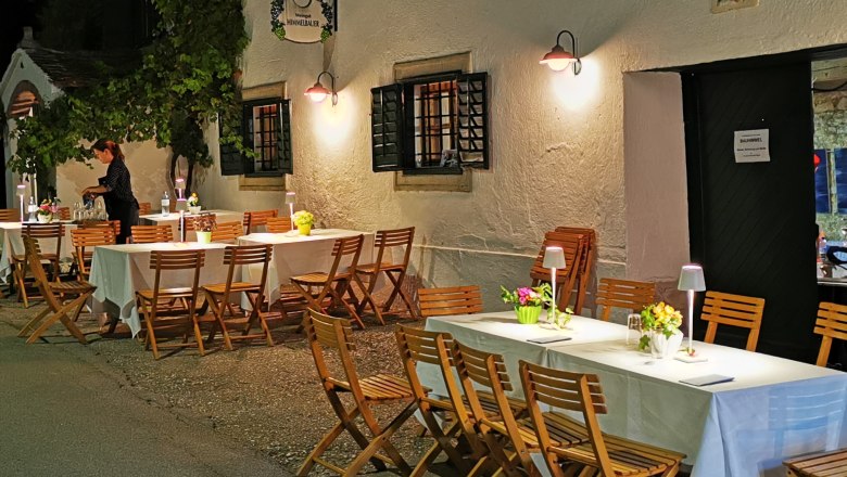 Idyllic atmosphere at the Himmelbauer winery, © Weinstraße Weinviertel Outdoor area of a wine cellar with set tables and wooden chairs at night.
