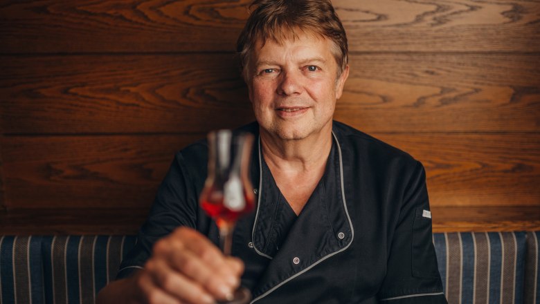 Landlord Josef Hofegger, © Niederösterreich Werbung/Daniela Führer A man in black clothing holds a glass of red drink in front of a wooden wall.