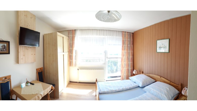 Guest room 1, © Gasthof Donaublick A cozy guest room with a double bed, wooden furniture, a small table and a TV on the wall.