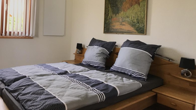 Bedroom, © Familie Mokesch A cozy bedroom with a double bed, grey bed linen, a painting on the wall and a window with blinds.