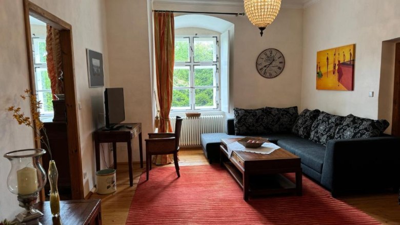 Vacation apartment, © Andrea Schubert Cozy living room with sofa, red carpet, chandelier and large window.
