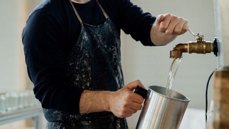 Candle manufactory, © Glaser Kerzen Person fills water from a tap into a metal container.