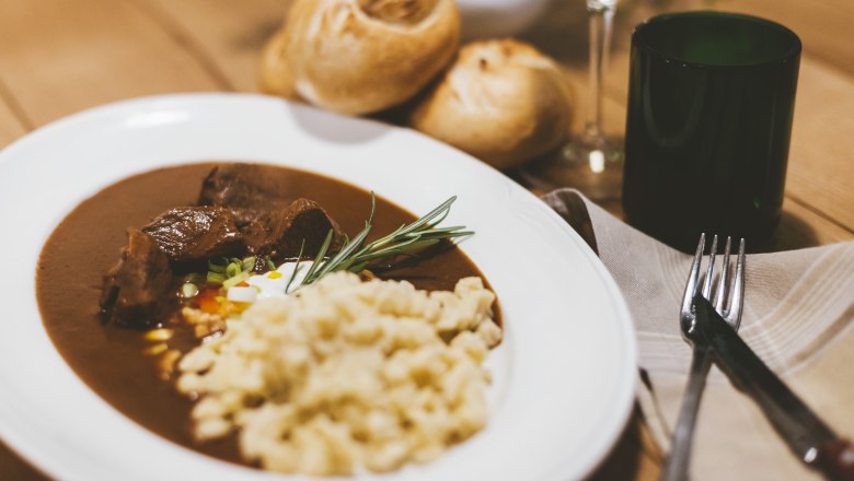 Creamy veal goulash with spaetzle, © Niederösterreich Werbung/David Schreiber Plate with goulash and spaetzle, bread and wine glass in the background.