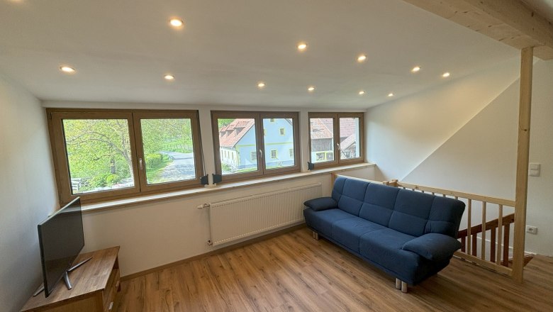 Hallway, © MIchael Hofer Living room with blue couch, wooden floor and large windows overlooking the outside.