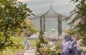Romantic impressions in the Ecolution.Lab, © Bernd Hochwartner A romantic garden with gazebo, green chairs and table, surrounded by trees and flowers.