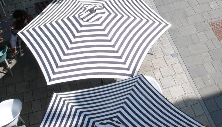 best place on the main square, © Süd - das Kulturcafé Two striped parasols on a paved square, photographed from above.