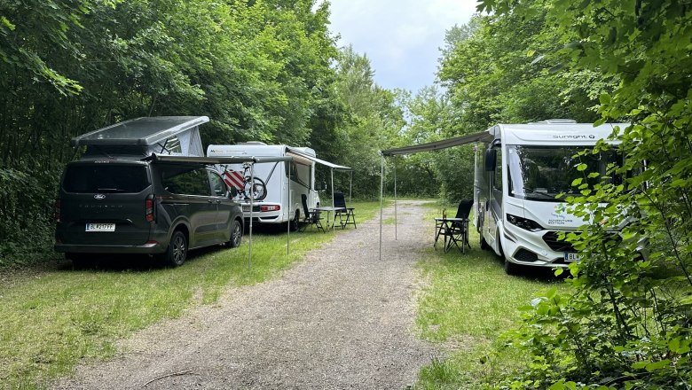 Camping Harrachpark, © Stadtgemeinde Bruck/Leitha Two motorhomes and a van on a campsite in the countryside with awnings and camping chairs spread out.