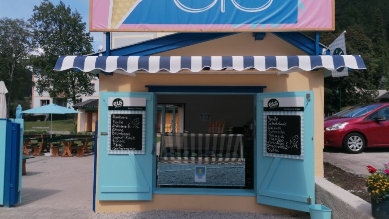 photo booth, © Gemeinde Gutenstein A small ice cream stand with blue shutters and an awning, surrounded by trees and cars.