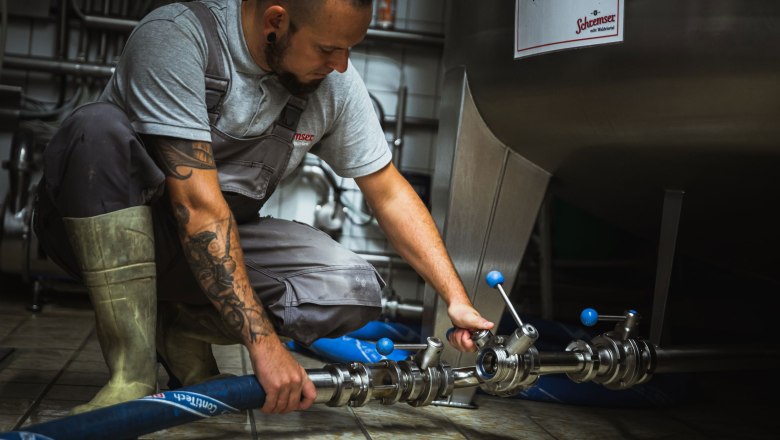 Brows, © Inge Funke A man in work clothes holds glasses of beer in front of a brewery.