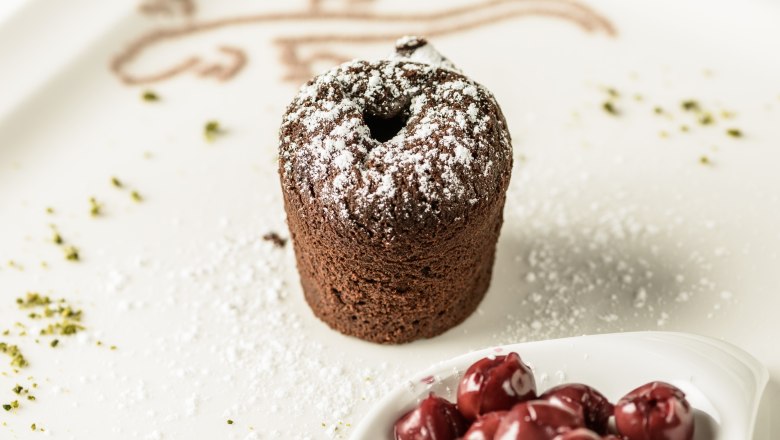 Dessert in the Genuss.Restaurant, © Rita Newman A chocolate cake with powdered sugar and cherries on a plate.