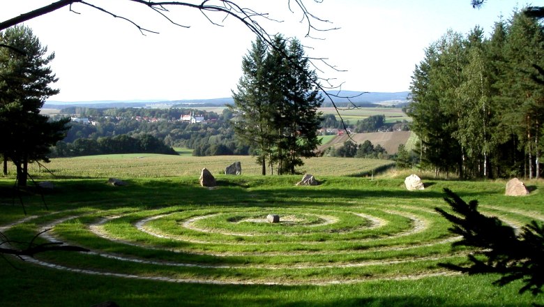 Arena Geomantica, © Naturpark Dobersberg A spiral labyrinth of grass and stones on a meadow with trees and a village in the background.