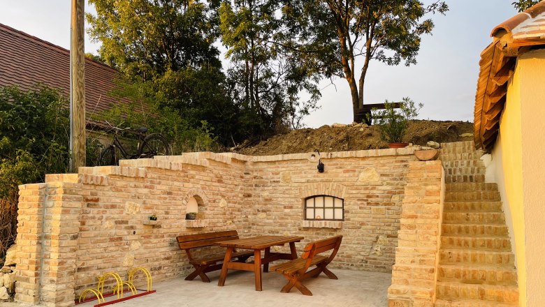 Outside seat, © Fam. Thürr Cozy outdoor area with wooden table and benches, surrounded by brick walls and stairs, in the evening light.