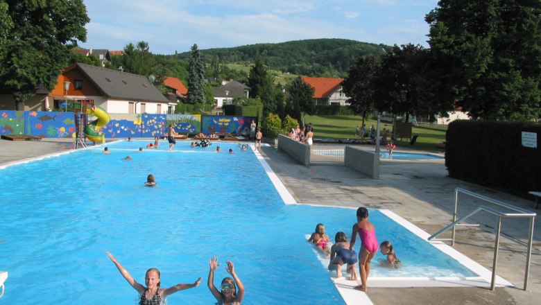 Outdoor pool Königstetten, © Donau Niederösterreich Outdoor pool with floats and slide, surrounded by trees and meadow.