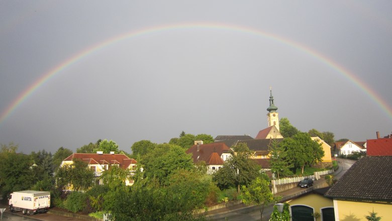 Rainbow over Gerersdorf, © Schild Renate A rainbow stretches over a village with a church and houses in Gerersdorf.