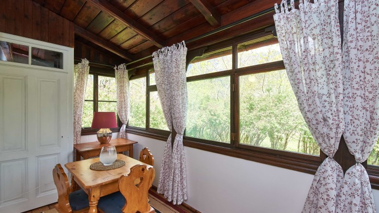 Top 5 - Conservatory, © VP FeWo OG A cozy winter garden with wooden furniture, floral curtains and a view of the greenery.