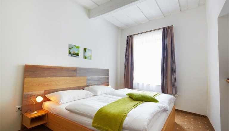 Standard double room, © Rathauskeller Melk Bright bedroom with double bed, green bedspread and two small pictures on the wall.
