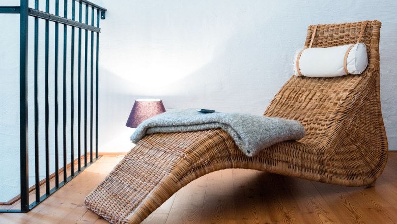 Reading corner, © Weinakademie Retz A cozy reading corner with a woven deck chair, a blanket and a lamp on a wooden floor.